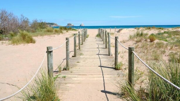 Un sentiero di legno che conduce a una spiaggia sotto un cielo sereno.