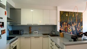Una cucina moderna con mobili bianchi, un forno a microonde, un tostapane e un lavello. Al muro, un quadro raffigura un gruppo di persone.