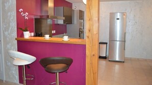 A kitchen with a pink accent wall, stainless steel appliances, and two bar stools. - Gîte des Patiasses, very spacious,between Rennes le Château and Rennes les Bains (Couiza)