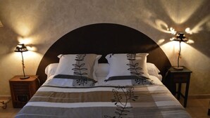 A neatly made bed with a striped bedspread and decorative pillows, flanked by two bedside lamps on wooden nightstands. - Gîte des Patiasses, very spacious,between Rennes le Château and Rennes les Bains (Couiza)