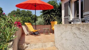 Una escalera de piedra que lleva a un edificio con un paraguas rojo, asientos al aire libre y vegetación.