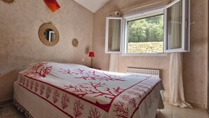 Un dormitorio con una cama, ventana, espejo y lámpara sobre una mesita de noche.