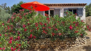 Un muro de piedra con flores rojas, un paraguas rojo y un edificio con paredes blancas y contraventanas grises.
