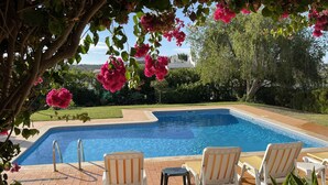 A swimming pool with two white chairs and a small table, surrounded by a tiled patio and lush greenery. - 3 bedroom Villa, Private Pool, Private Location. Close to Guia, Near Albufeira Beaches & Old Town. (Guia)