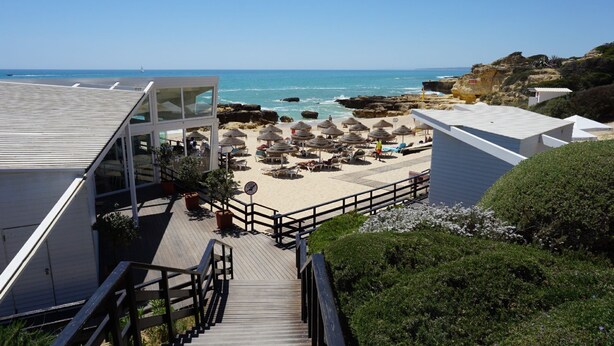 A beachside hotel with a wooden staircase leading to a deck with beach umbrellas and lounge chairs. - 3 bedroom Villa, Private Pool, Private Location. Close to Guia, Near Albufeira Beaches & Old Town. (Guia)