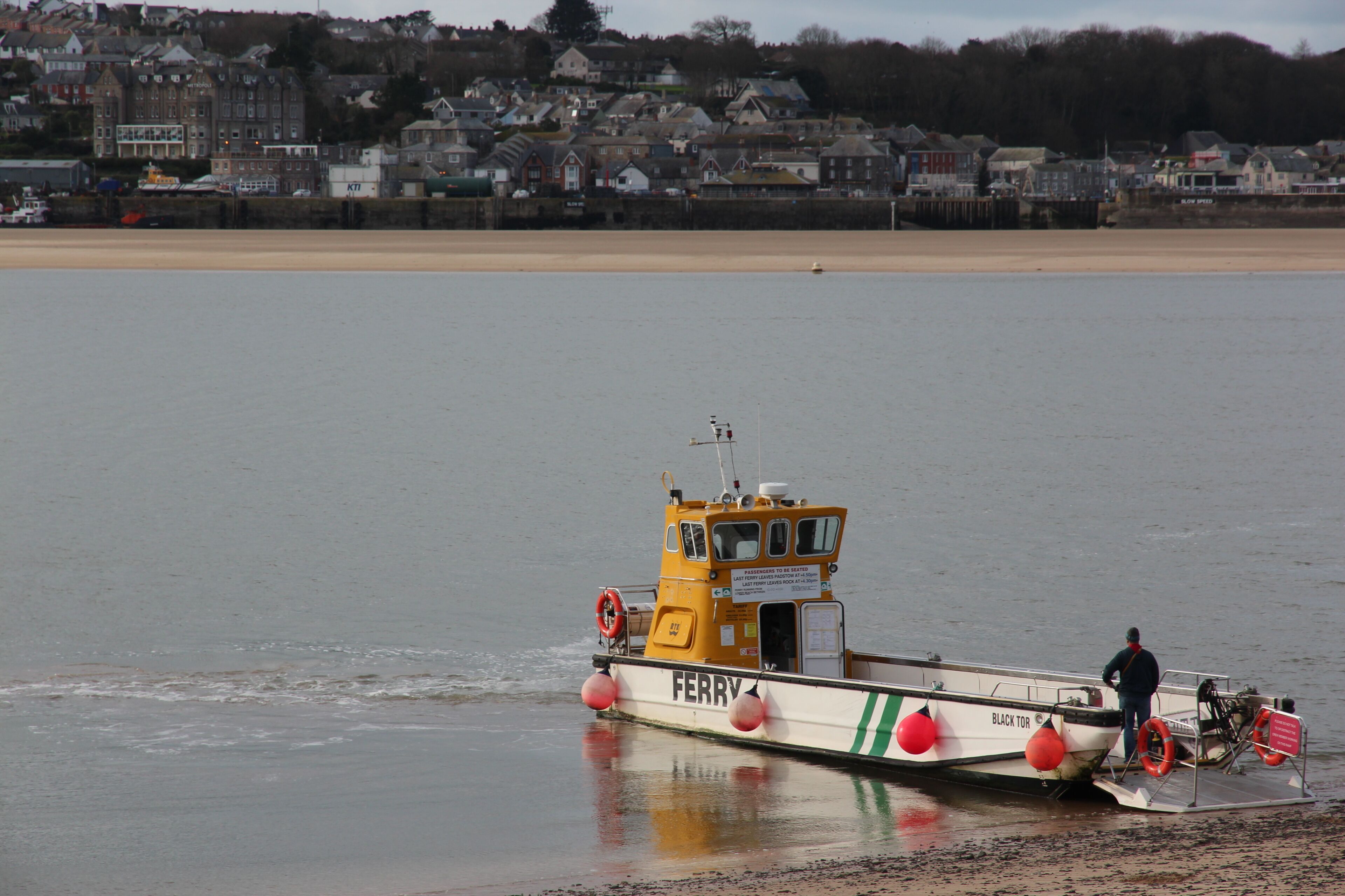 A ferry boat named "FERRY BLACK TOR" docked at a beach with a town in the background.