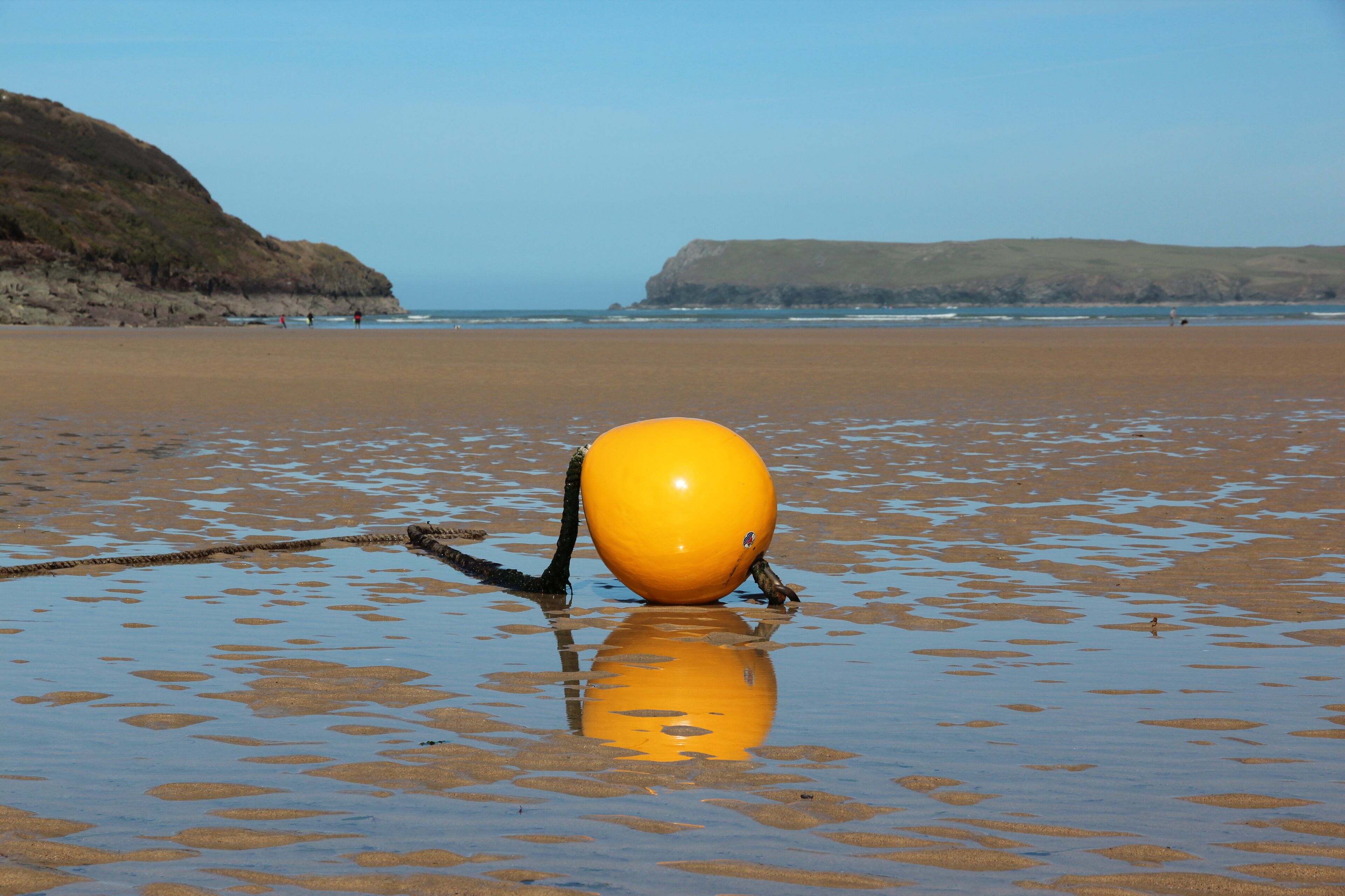 A beach with a large yellow buoy in the water.