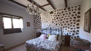 Een slaapkamer met een stenen muur, een bed met een geborduurd beddegoed, een kroonluchter en een naaimachine.