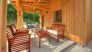 Un patio exterior de madera con mesa y sillas, un sofá y una ventana.
