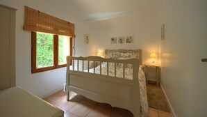 Un dormitorio con una cama, una ventana con persianas, una mesita de noche con lámpara y una obra de arte en la pared.