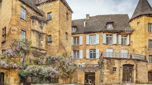 Un edificio histórico de piedra con múltiples ventanas y un balcón, rodeado por un patio.