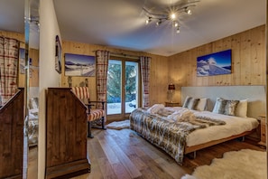 Une chambre aux murs lambrissés, avec un grand lit, un fauteuil et une vue sur un paysage enneigé par la fenêtre.