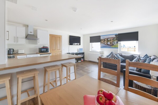 A modern kitchen with white cabinets, a wooden countertop, and a dining area with a table and chairs. There is a sofa and a window with a view of the outside. - Sparkling Clean Fabulous views of Stirling Castle (Stirling)