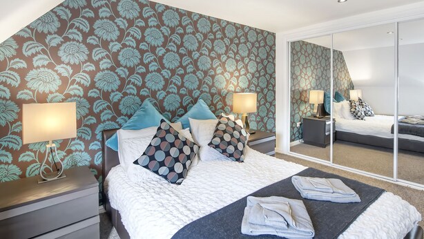 A hotel room with a large bed, two bedside tables with lamps, a mirror, and a patterned wallpaper. - Sparkling Clean Fabulous views of Stirling Castle  (Stirling)