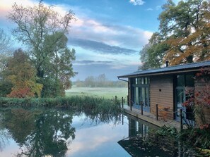 A wooden building with a glass door, surrounded by trees and a calm body of water.