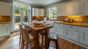 Una cocina moderna con armarios blancos, una isla de madera y un comedor con dos taburetes.