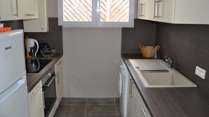 Eine kompakte Küche mit Einbauofen, Spüle und einem Fenster über der Arbeitsfläche.