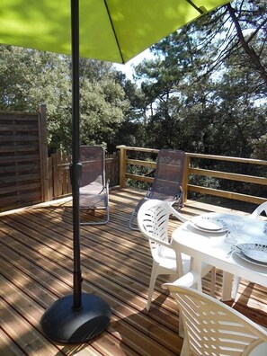 An outdoor deck with a table set for dining, surrounded by chairs, and a large umbrella providing shade. - House 6/8 people, 100m from the beach, on the edge of Longeville's Forest (La Tranche-Sur-Mer)