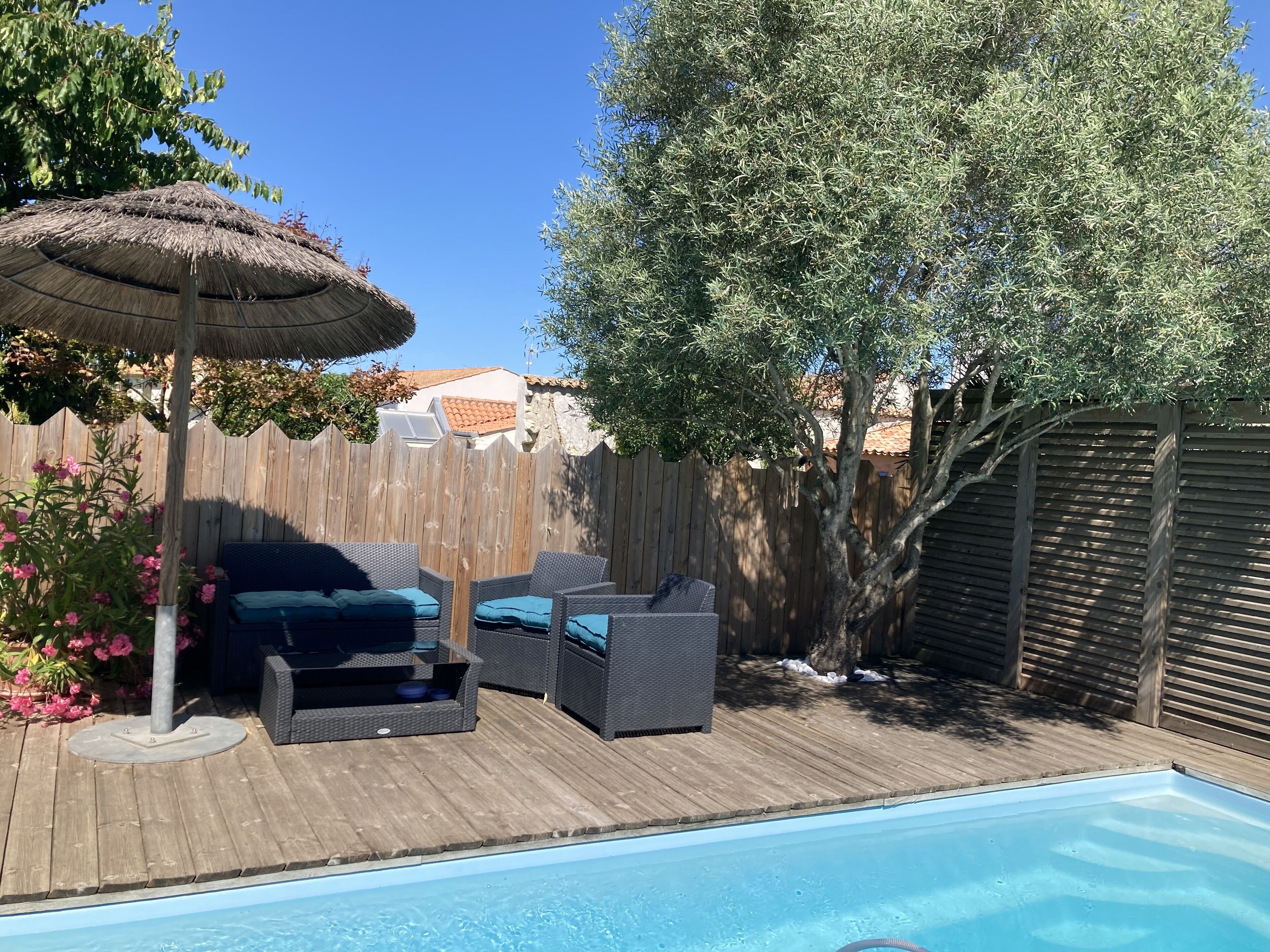 Un giardino sul retro con piscina, terrazza in legno, mobili da esterno e recinzione di legno.