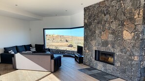 Un salon moderne doté d’une cheminée en pierre, de grandes fenêtres et offrant une vue sur le paysage désertique.