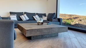 Un salon moderne avec un canapé gris, une table basse en bois et une grande fenêtre donnant sur un paysage désertique.