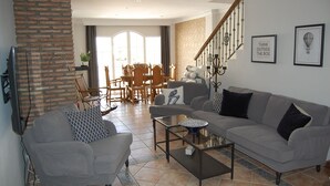Ein Wohnzimmer mit zwei grauen Sofas, einem Couchtisch und einem Essbereich mit Holzsesseln und einem Tisch.