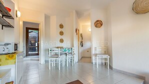 A spacious living area with a dining table and chairs, a kitchen area with appliances, and a hallway leading to a door. - Ambra: holiday house with shared pool (Costa Paradiso)