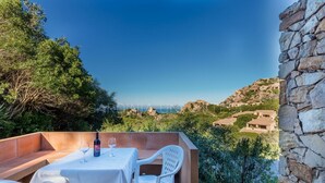 A terrace with a table and chairs, overlooking a coastal landscape with stone buildings. - Ambra: holiday house with shared pool (Costa Paradiso)