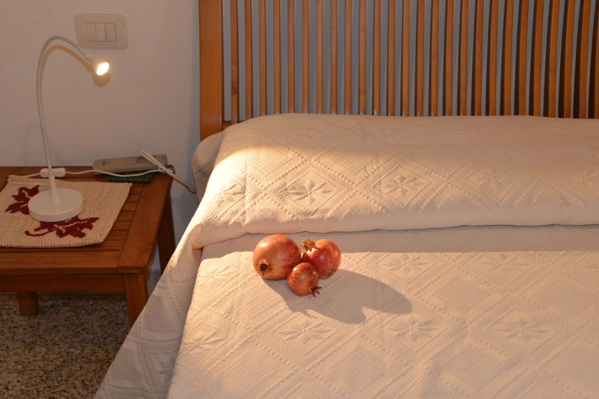 A neatly made bed with a white quilt, a bedside lamp, and a woven placemat with a red leaf design.