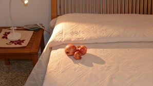 Una cama bien hecha con colcha blanca, una lámpara de noche y un protector de mesa tejido con diseño de hoja roja.