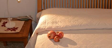 A neatly made bed with a white quilt, a bedside lamp, and a woven placemat with a red leaf design.