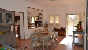Un salón espacioso con una gran mesa de comedor de madera, varias sillas, un sofá y una zona de cocina con armarios y estufa.