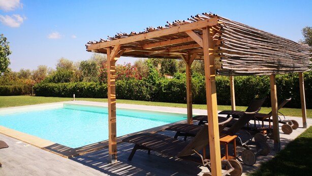 Una piscina con una pérgola de madera y sillones de descanso.