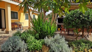 Un patio con un edificio amarillo, mobiliario exterior y diversas plantas.