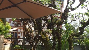 Un patio con un amplio paraguas, dos sillas y un césped cuidado.