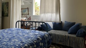 Un dormitorio con cama, mesita de noche, silla, ventana con cortinas y vista a zonas verdes.