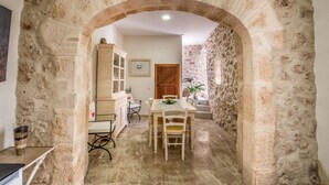 Un arc en pierre mène à un espace repas comprenant une table et des chaises, un buffet et une porte.