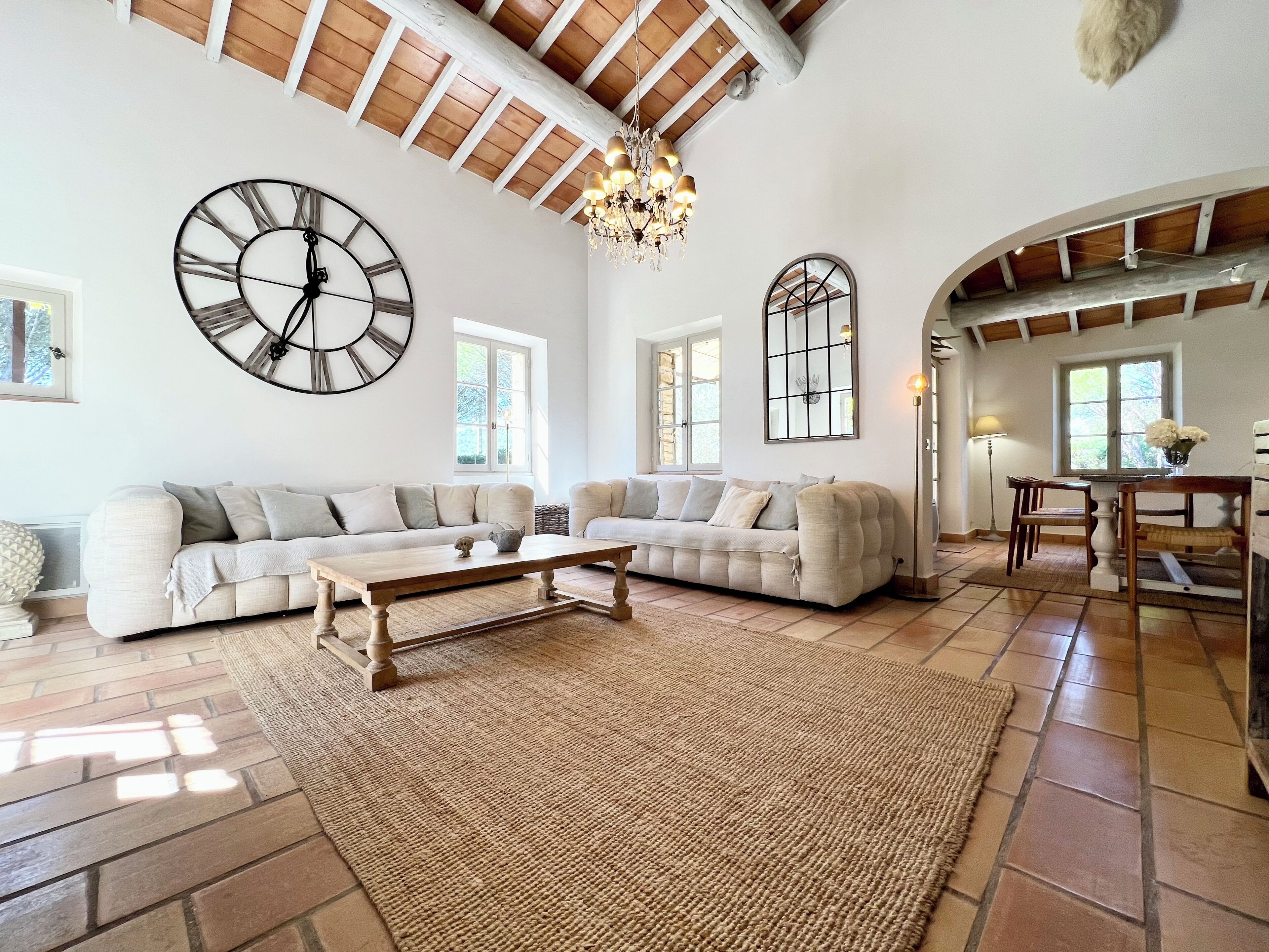 A spacious living room with a large sectional sofa, a wooden coffee table, and a large wall clock.