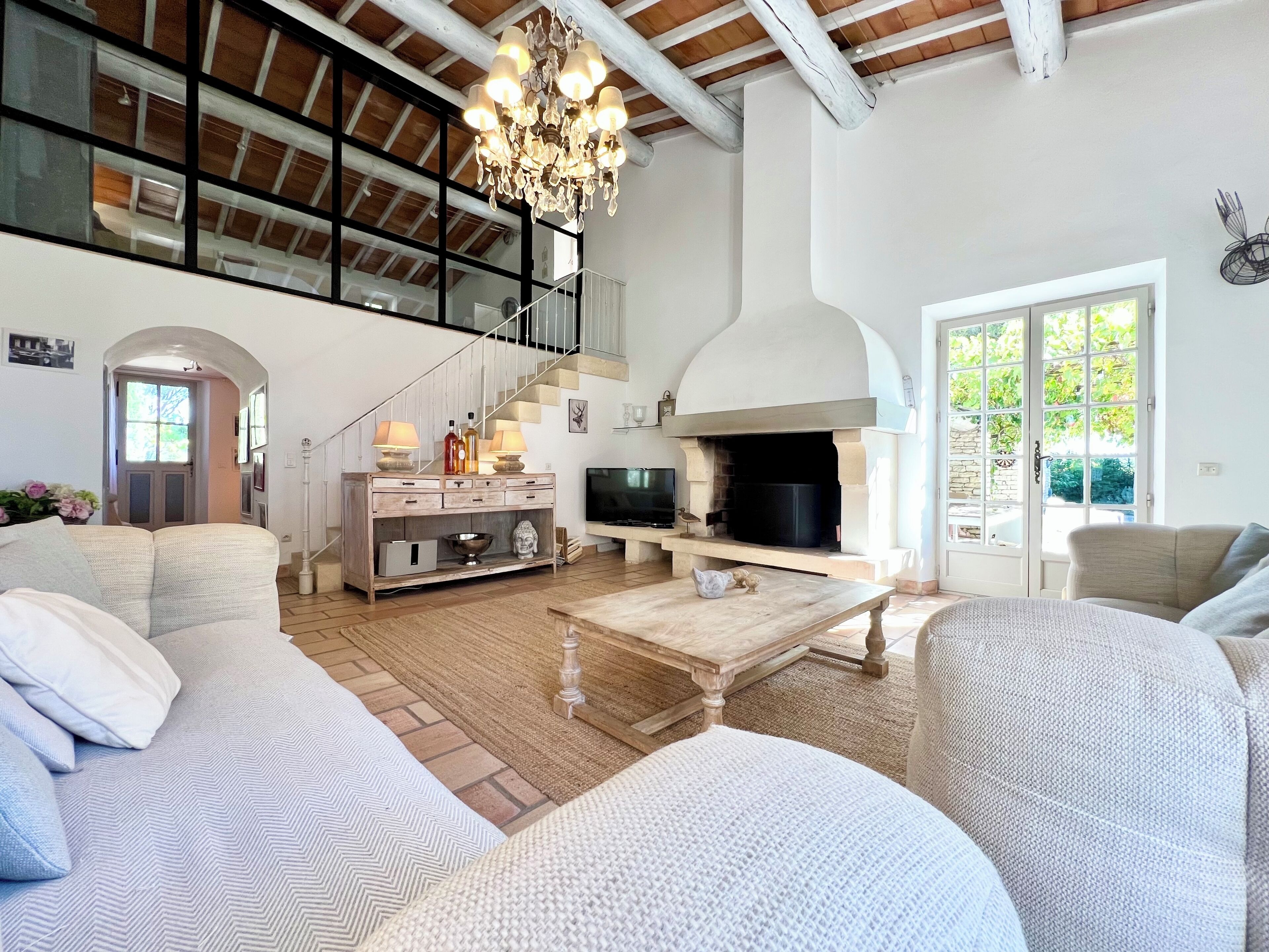 A spacious living room with a high ceiling, a fireplace, a staircase, and a large window.