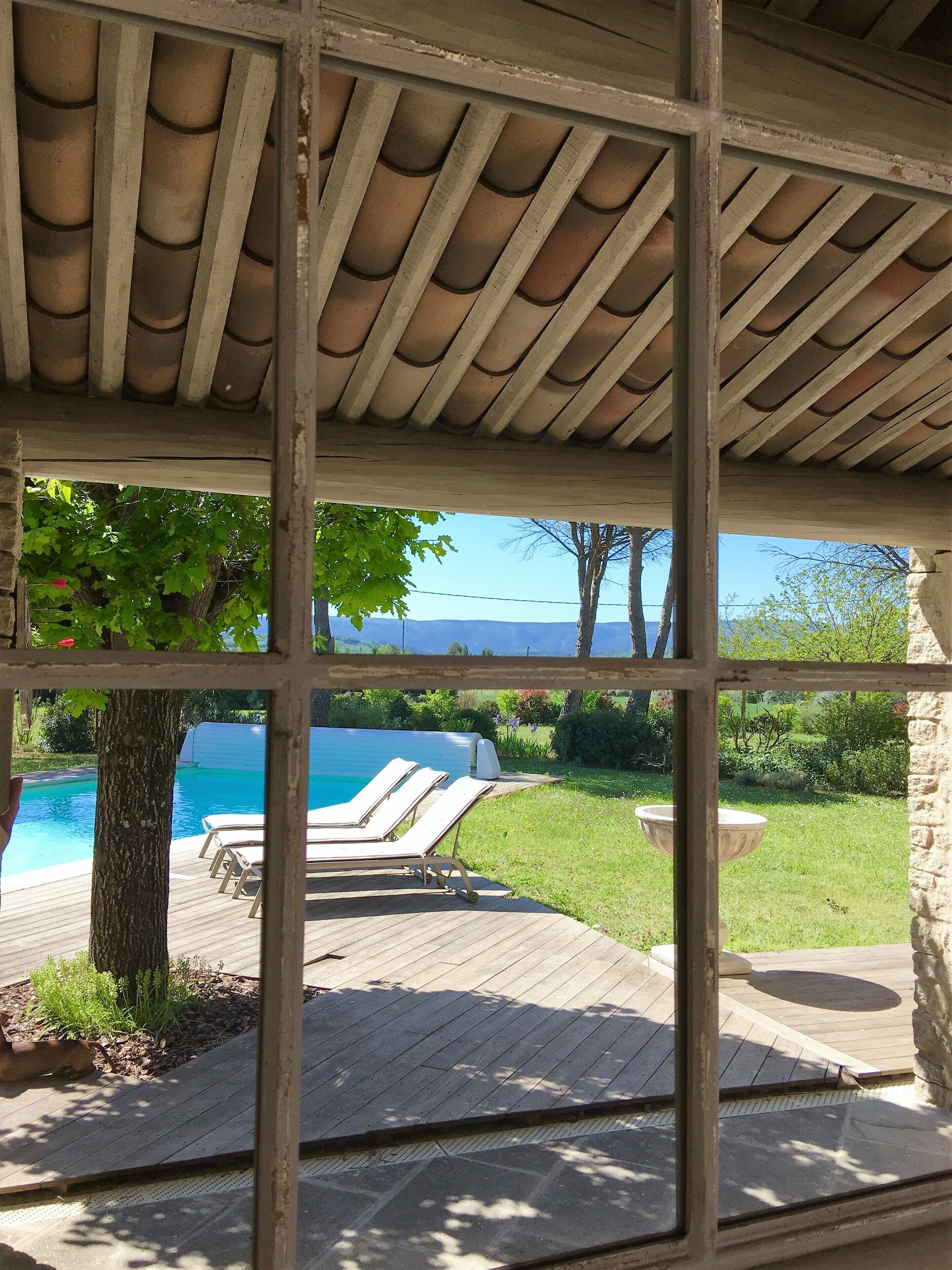 A covered outdoor area with a pool, lounge chairs, and a view of a mountainous landscape.
