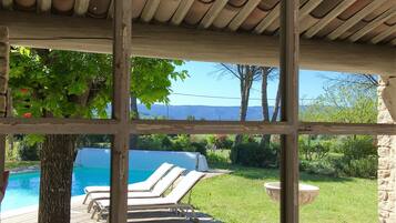 A covered outdoor area with a pool, lounge chairs, and a view of a mountainous landscape.