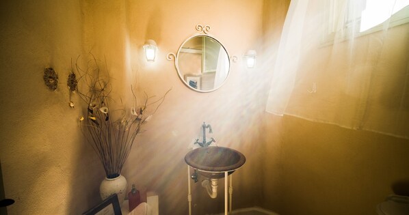 A bathroom with a round mirror, a pedestal sink, and a vase with dried flowers.