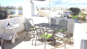 Una terrazza con tavolo e sedie, un ombrellone e vista sulla città e sul porto turistico.