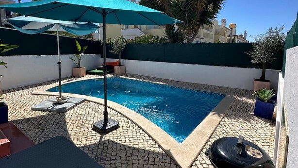 Una piscina con bordo piastrellato, un barbecue e un ombrellone.