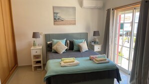 Una camera da letto con un letto, comodini, un mobiletto notte, un condizionatore d'aria a parete e una finestra con tende.
