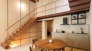 Een moderne keuken met een centraal eiland, een eethoek met een ronde tafel en stoelen, en een trap naar een hoger niveau.