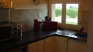 A kitchen with a microwave, kettle, and coffee maker on the counter, a window with a view of greenery, and a wall clock. - Peaceful Gite + PRIVATE Pool Exclusively for you +Magnificent Panoramic Views  (Lalanne)