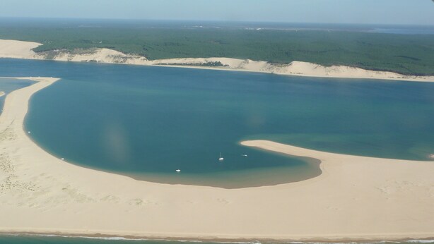 An aerial view of a coastal area with a large body of water, sandy beaches, and a forested area in the background.