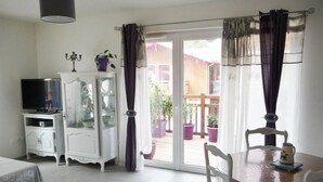 A room with a dining table, chairs, a television on a cabinet, and a sliding glass door leading to an outdoor area with potted plants.