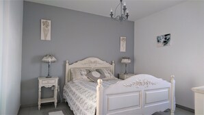 A bedroom with a white bed, two bedside tables with lamps, a chandelier, and artwork on the walls.